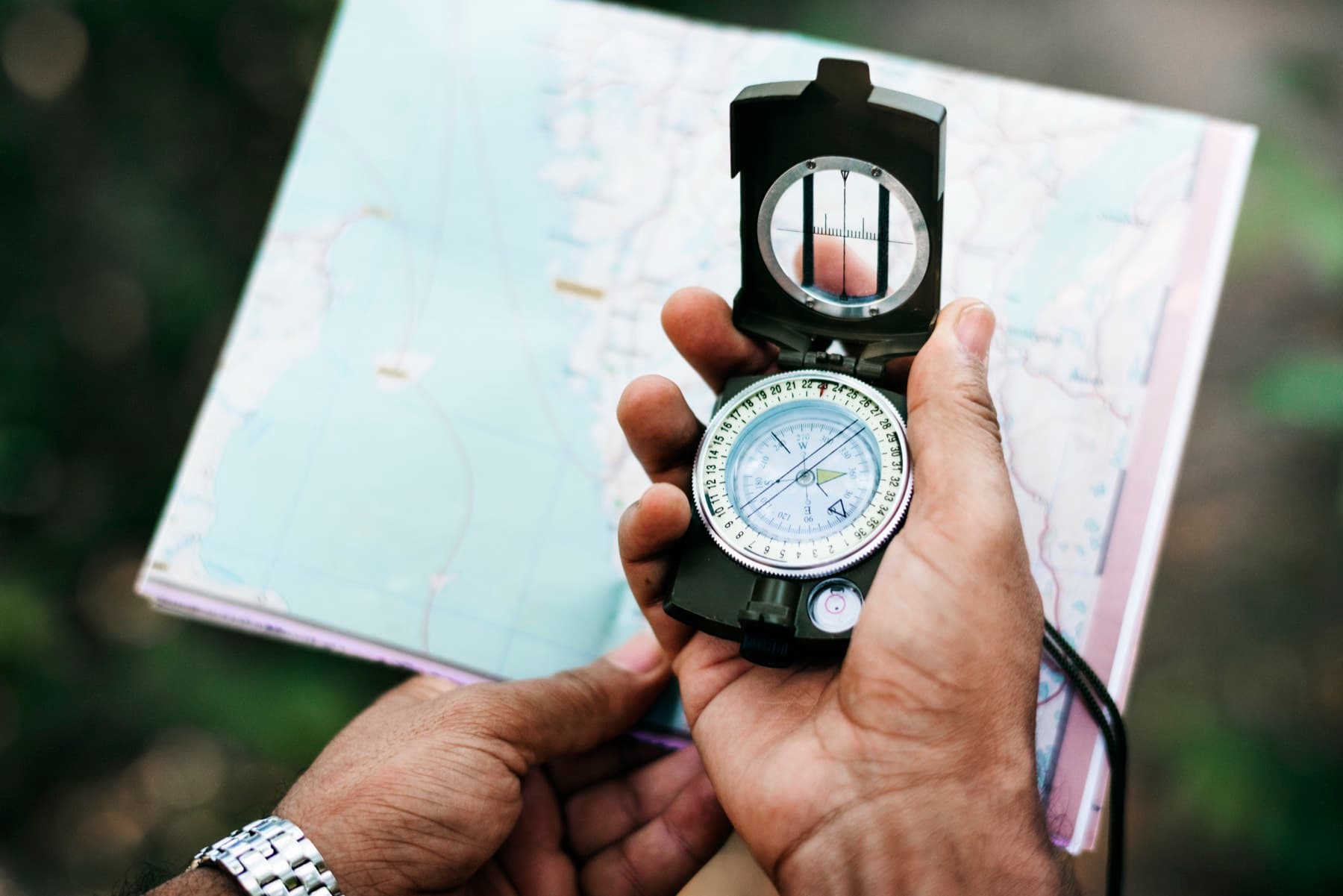 Hands holding a sighting compass over an unfolded topographic map
